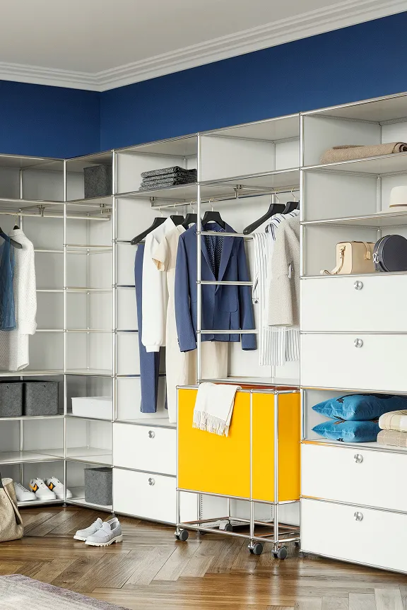 Offenes USM Haller Regalsystem in Weiß mit Kleiderstangen, Schubladen und Boxen vor blauer Wand.